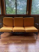 Front view of vintage wrought iron patio sofa with three orange cushions showing sun fading.
