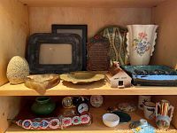 Shelf with pottery plate, picture frames, decorative plaque, vase, ashtrays, clocks and small decorative items arranged.