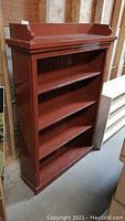 Full view of wooden bookshelf showing four shelves and raised edge top, painted brown with some paint chipping.