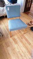 Front view of mid century modern chair showing blue upholstered seat and backrest on wooden legs against a wood floor.