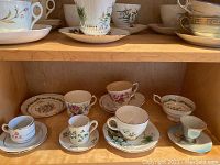 Shelf display with an assortment of cups and saucers, showing various floral and classical patterns and multiple sets and loose items.