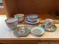 Six assorted oriental and Japanese tea cups, saucers, and bowls arranged on a table.