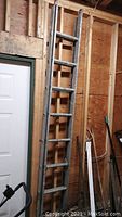 Front view of the 14 foot aluminum extension ladder leaning against a wooden frame wall next to a door, showing the overall structure and condition.