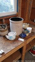 Overview of all ceramic items including the large crock, small pitchers and assorted planters arranged on wooden table, showing condition and size.