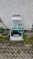 Front view of light green plastic hose reel with green garden hose partially wound around it, placed outside against a grey wall.