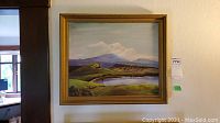 Full view of the framed oil painting showing a scenic landscape with hills and a body of water.