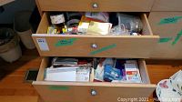 Two wooden drawers filled with assorted office supplies and stationery items, visible are envelopes, sticky notes, batteries, and various small packs.
