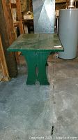 Front view of green wooden table showing the thick base with decorative cutout and paint wear.