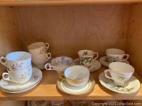 Full view of four matching cups and saucers with gold floral design, Delphine floral cups and Noritake scenic cup on shelf