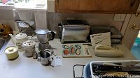 Photo of kitchen counter with all items including toaster, slicer, waffle maker, teapot, milk frother, stovetop espresso maker, and cookbook arranged.