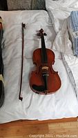 Violin and bow laid out on bed with case partially visible