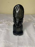 Front view of the black onyx sculpture showing carved human face and headdress with leaf patterns, smooth polished surface.