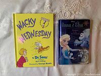 Two children's books: Wacky Wednesday by Dr. Seuss and Anna & Elsa Return to the Ice Palace by Disney shown side by side on white fabric.