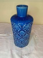 Full front view of the blue ceramic flower vase showing the textured ornamental pattern and shiny finish.