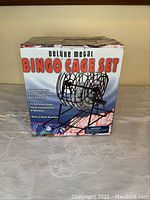 Front view of boxed deluxe metal bingo cage set showing image and product features on packaging