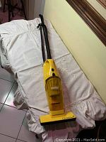 Full view of yellow Eureka upright vacuum cleaner laid flat, showing handle, dust container, and base.