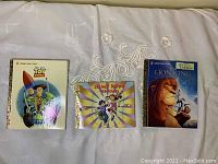 Three children's books side by side: Toy Story, Jump Rope Rhymes, and The Lion King on a white fabric background.