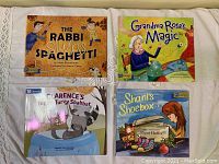 Four Jewish children's books arranged on a surface: The Rabbi Slurps Spaghetti, Grandma Rose's Magic, Clarence's Torsy-Turvy Shabbat, and Shani's Shoebox.