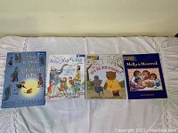 All four children's books laid out on a bed sheet, showing full front covers including titles and artwork.