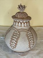 Front view of the terracotta vase with lid, showing leaf decorations and sculpted finial.