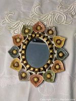 Front view of decorative wooden mirror with colorful flower petal design and oval reflective surface.