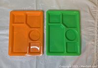 Two plastic compartment plates, orange and green, laid side by side, showing compartment design and size