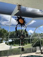 Metal and glass sun-themed wind chime hanging outdoors with several hanging bells and sun and moon motifs.