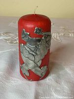 Clear frontal image of red Christmas candle with pewter Santa Claus figurine attached.