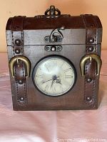 View of the small wooden chest box showing clock with stained plastic cover, metal latch closure, and faux leather straps.