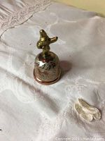 Photo of the small copper bell with bird figure on top showing detailed engravings on the surface.