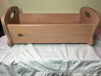 Front view of small wooden rocking cradle, showing rectangular shape, rocker legs, and cutout handles on end panels.