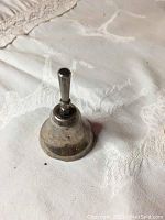 Small silver bell showing side angle and handle detail on a light patterned fabric background.