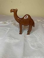 Front and side view of the small wooden camel figurine showing its shape and polished surface with a visible stain on the snout.