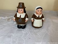 Front view photo of the pilgrim man and woman ceramic salt and pepper shakers on a cloth background.