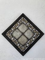Metal square wall decor with four central raised square tiles and leaf border in a black frame, showing weathered and aged metal texture.