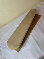 Image of long and narrow sleeve ironing board with beige padded surface and rounded ends on one side.