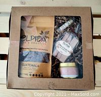 Gift box containing Elpida Guatemala coffee, lip balm, soap, and candle shown inside brown cardboard box with clear window.