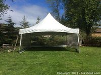 Photo of a white 20x20 peaked party tent standing on grass with transparent side panels visible.