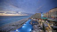 Beachfront resort exterior with large lagoon pool and ocean view at sunset.