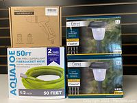 Package with green 50 ft garden hose, black gun sprinkler nozzle box, and two boxes of Patriot Lighting Cranford solar LED landscape lights.