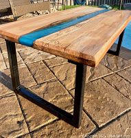 Angled view showing maple wood grain, blue-green epoxy river detail, and black metal legs