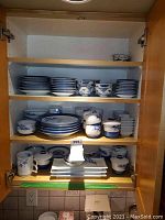 Full cabinet view with four shelves of mixed blue and white porcelain dishware including plates, bowls and mugs.