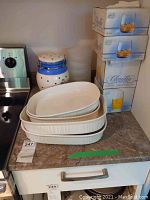 Three white ceramic baking dishes stacked on kitchen counter next to white ceramic coffee canister with blue lid and accents