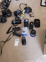 Overview of lot on carpet showing four cameras, two flashes, one grip, one third-party lens, assorted cases and filters