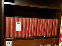 Full front view of the 18 red hardcover Chinese books lined up on a bookshelf, showing gold Chinese text on spines and volume numbers.