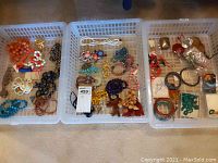 Overview of three plastic bins containing assorted necklaces and bracelets