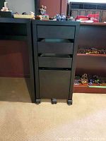 Front view of the black rolling four-drawer filing cabinet showing its compact size and casters.