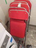 Stacked view of 5 red folding chairs showing padded seats and backs with chrome metal frames
