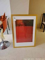 Full view of framed art print leaning against wall next to chairs and table.