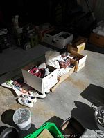 Wide view of lot showing boxes containing golf balls, golf shoes, hats and visors in a garage setting.